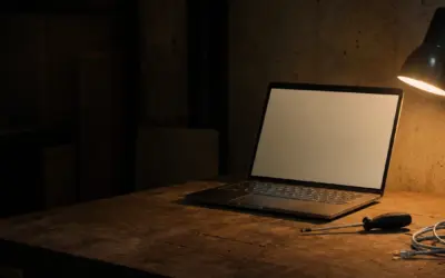 Un portatile aperto sul banco da lavoro accanto a un cacciavite e a un cavo di rete